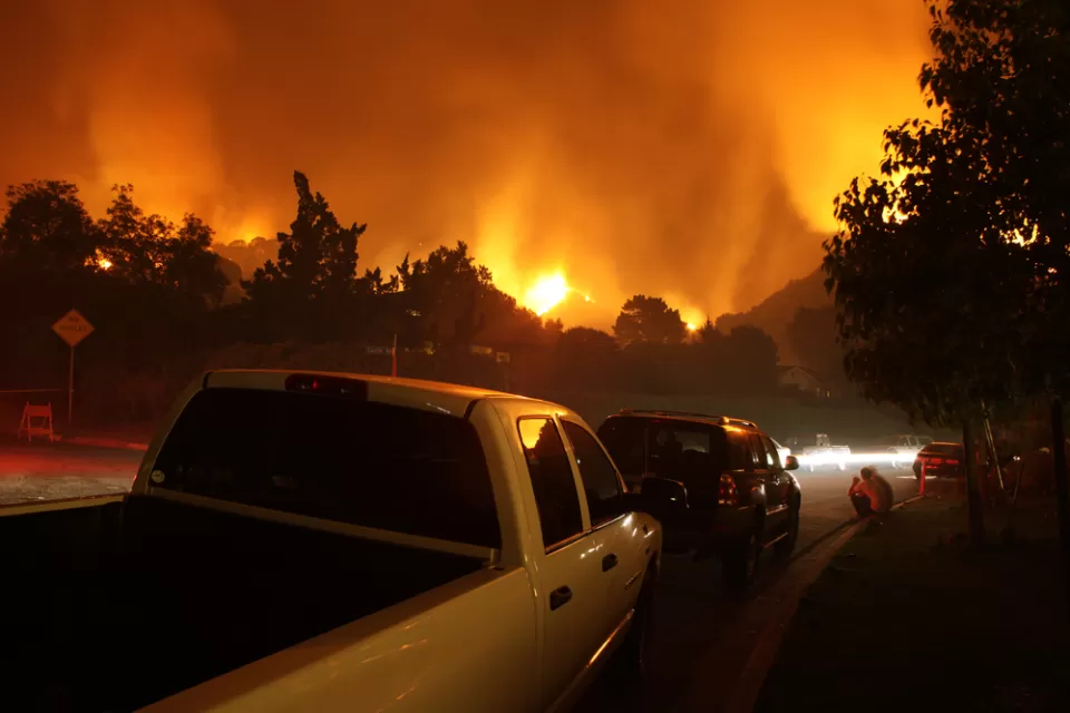Cars lined up on a street with fire burning in background